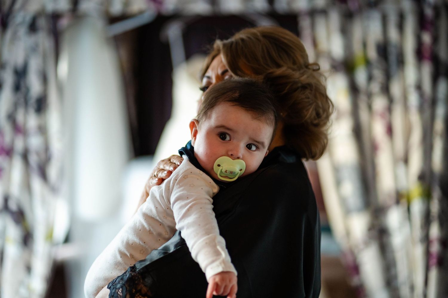 Young child in white clothing being held up against a blurred background.