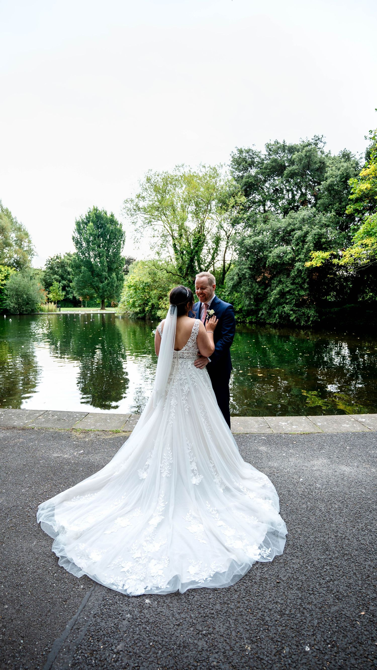 A romantic wedding portrait by a lake showing the bride's detailed lace dress train.