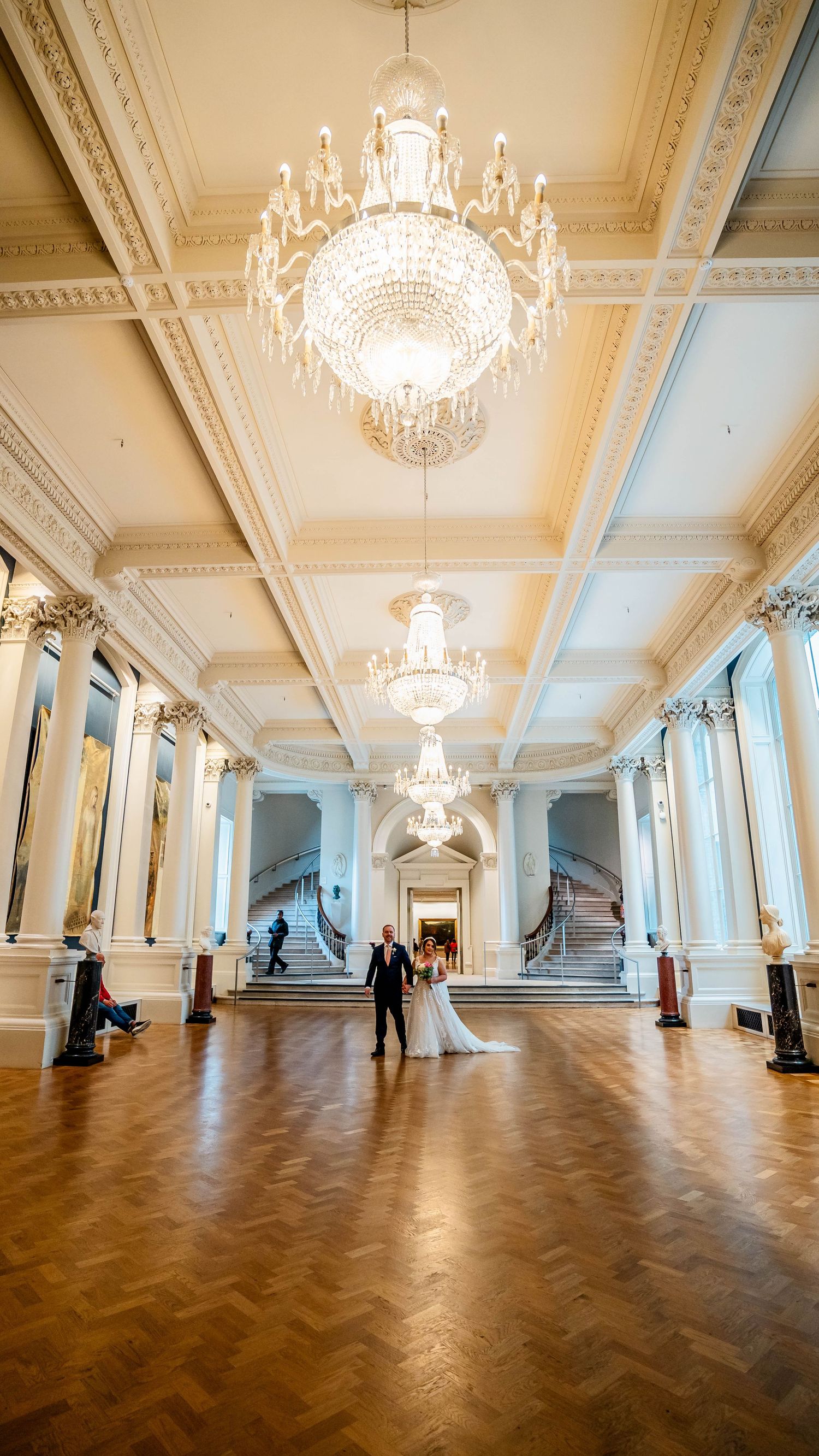 Majestic white ballroom features multiple crystal chandeliers and herringbone wood flooring.
