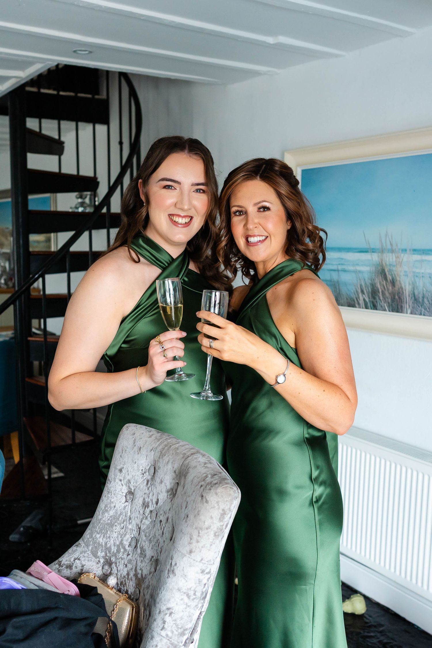 Two people in green dresses pose together for photos in front of a spiral staircase.
