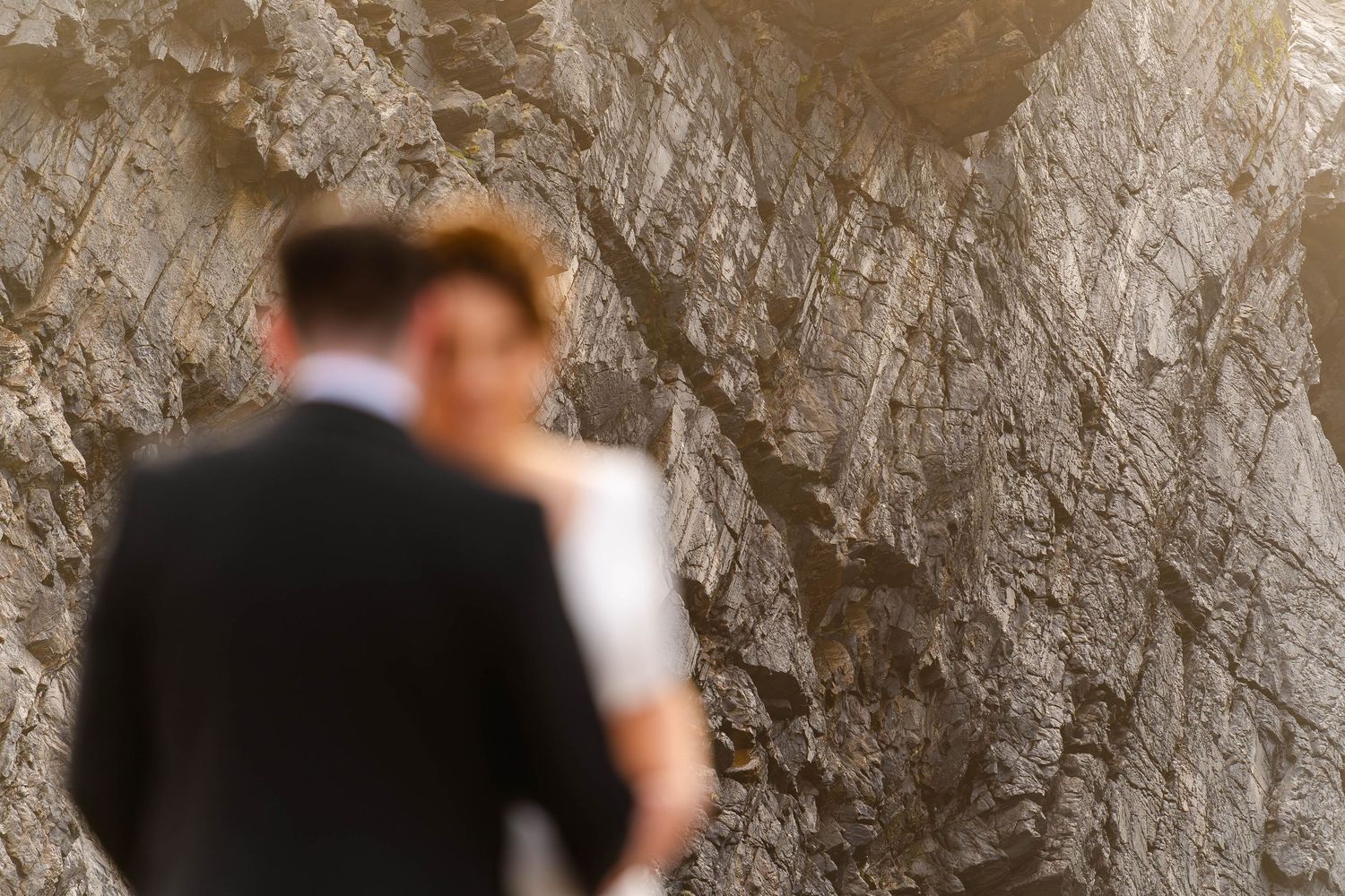 A couple shares an intimate moment during their wedding ceremony against a rustic backdrop.