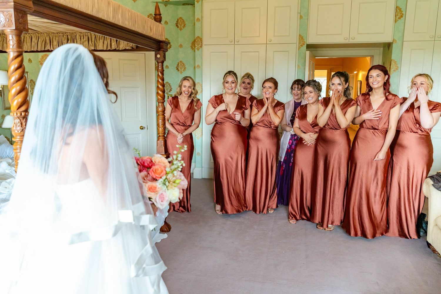 Wedding party in matching dusty rose dresses poses together in an elegant indoor venue with white walls and decor.