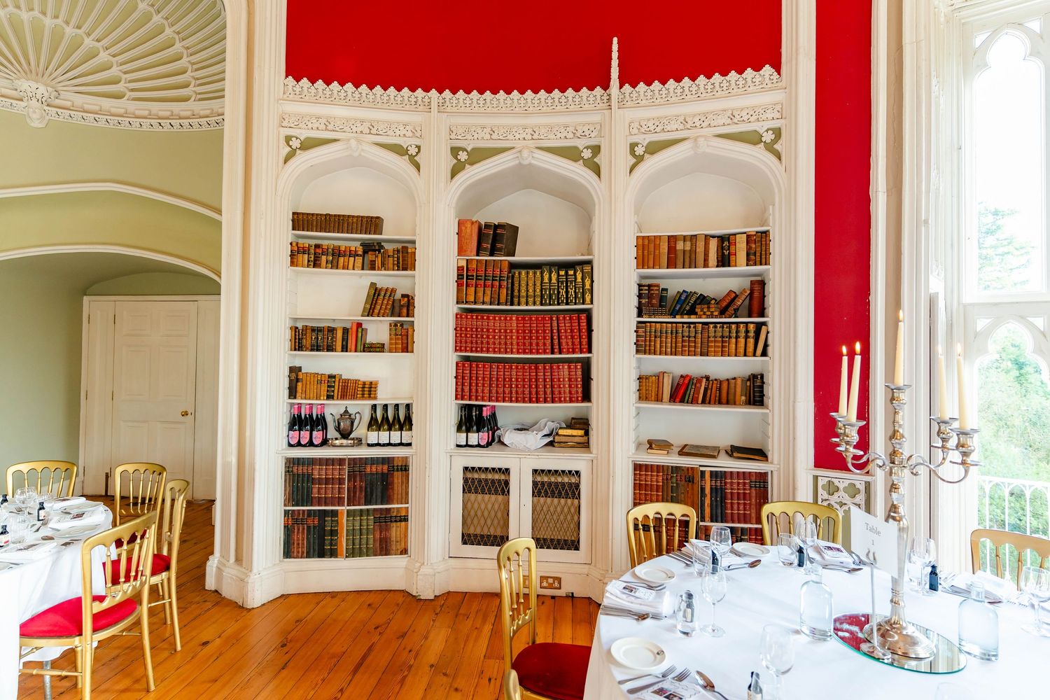 Elegant dining room with built-in white bookshelves, red accent wall, and arched windows in a panoramic view.