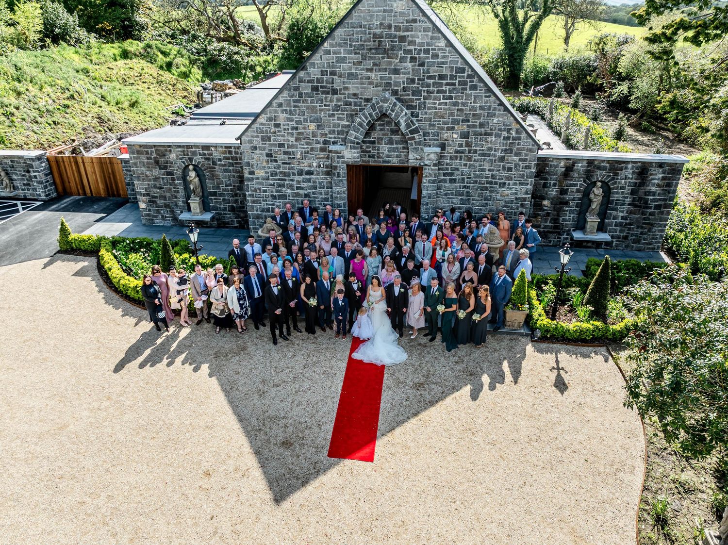 Large group gathering outside a historic stone building with a red door.