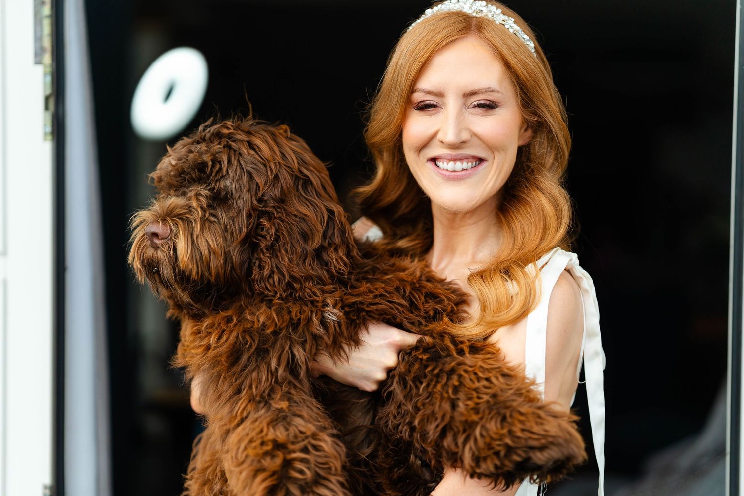 Brown fluffy dog being held in a joyful embrace against dark background.