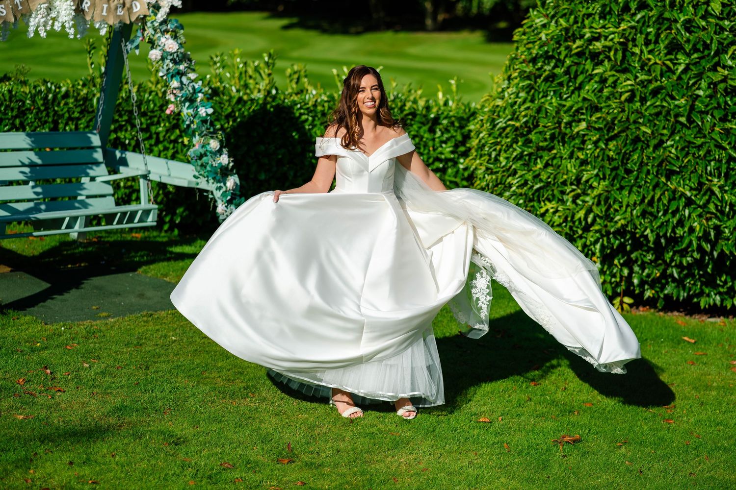 Bride's white dress flows dramatically during outdoor garden photo session.