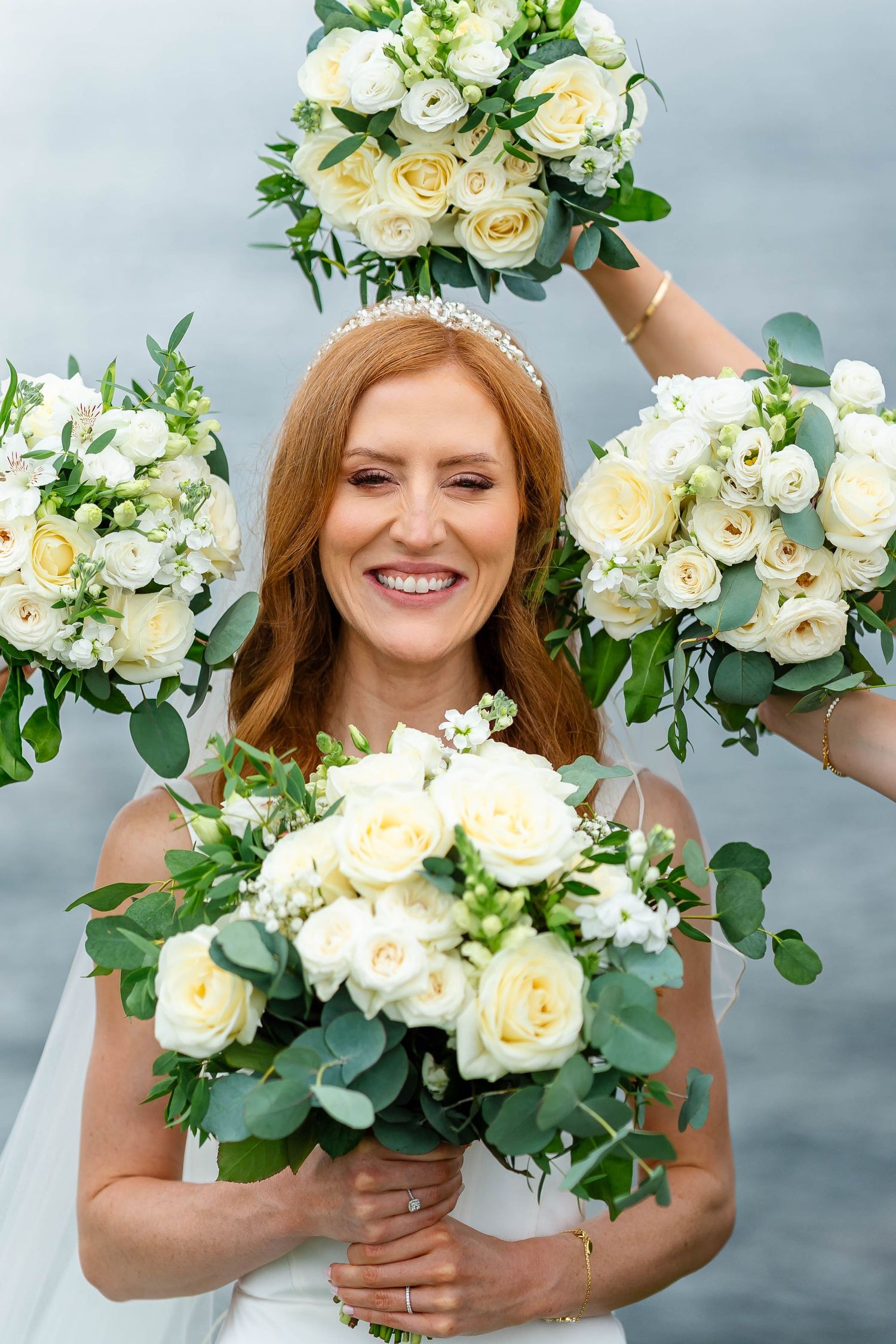 Beautiful white rose and eucalyptus wedding bouquets displayed against a cloudy coastal backdrop.