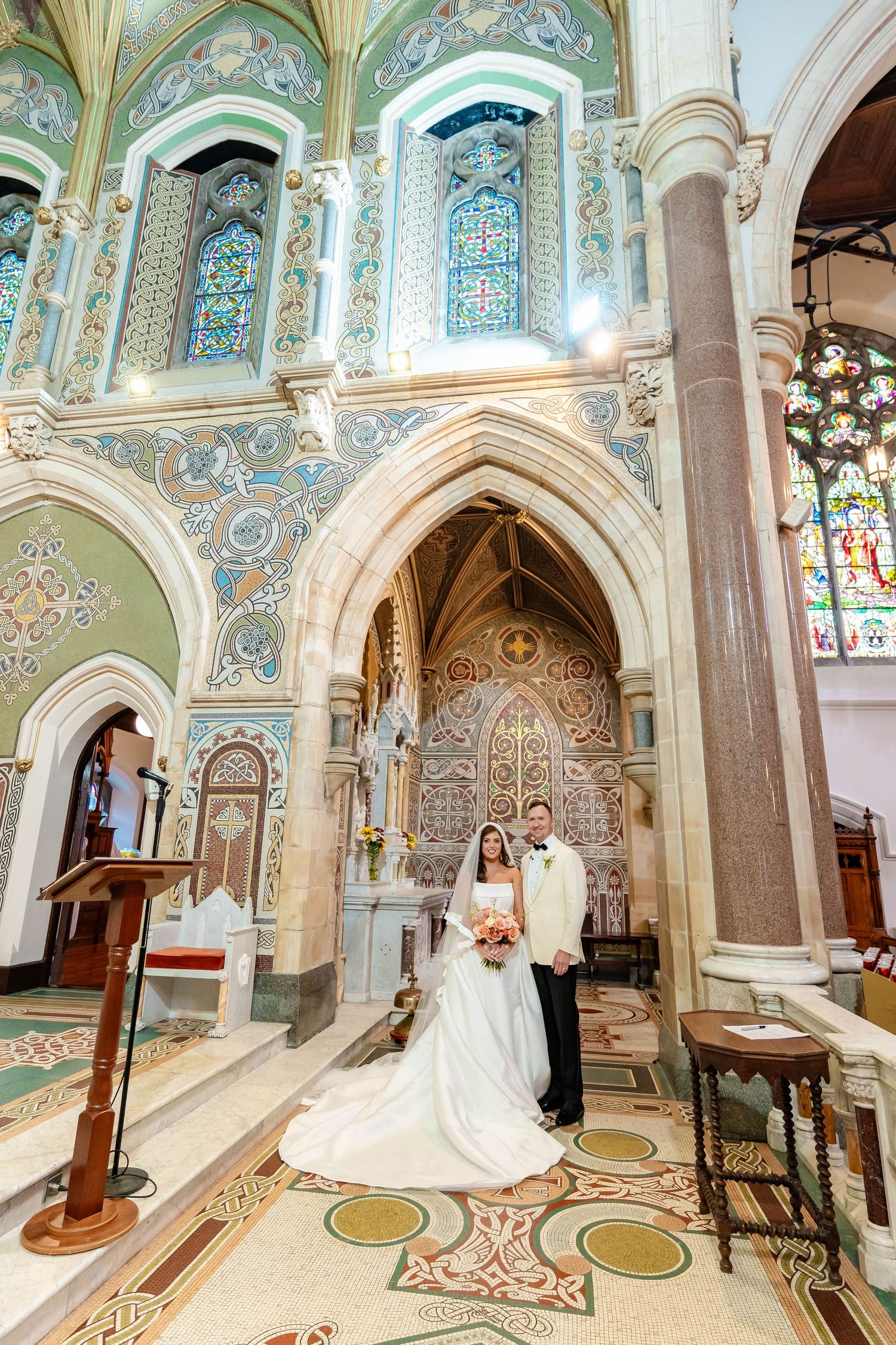 Ornate church interior with elegant arches, stained glass windows, and decorative painted walls in soft pastel colors.