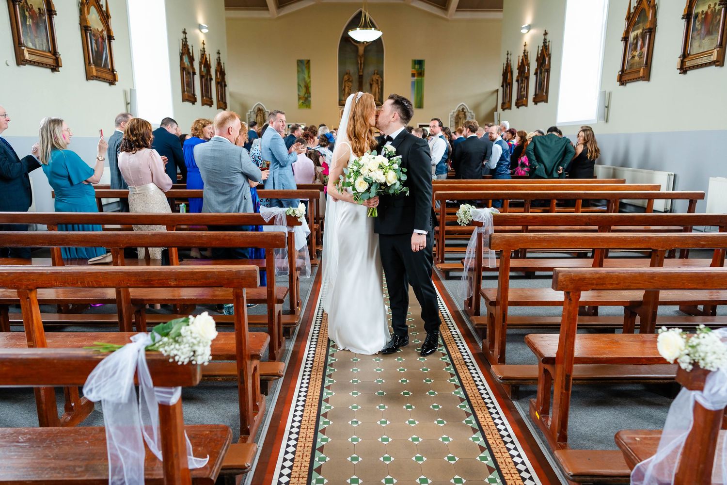 Interior of church sanctuary with wooden pews and patterned carpet runner.
