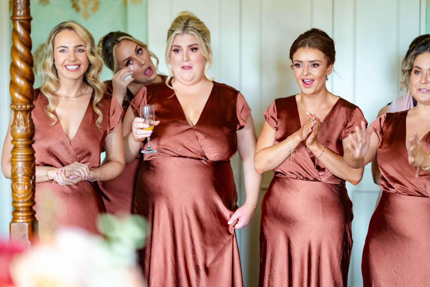 A row of bridesmaids wearing matching dusty rose satin dresses pose together at a wedding celebration.