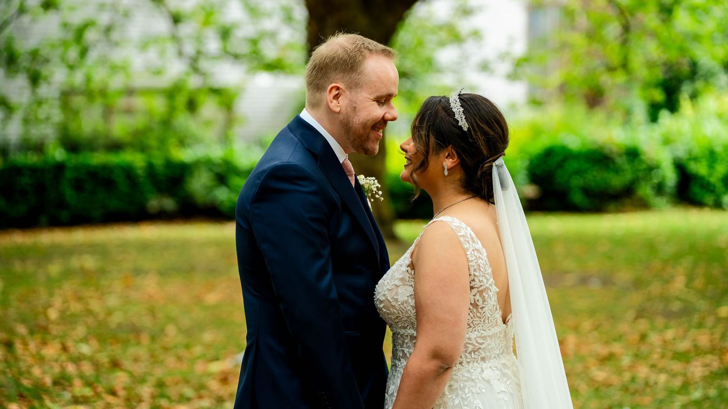 A wedding couple shares an intimate moment in a lush green garden setting.