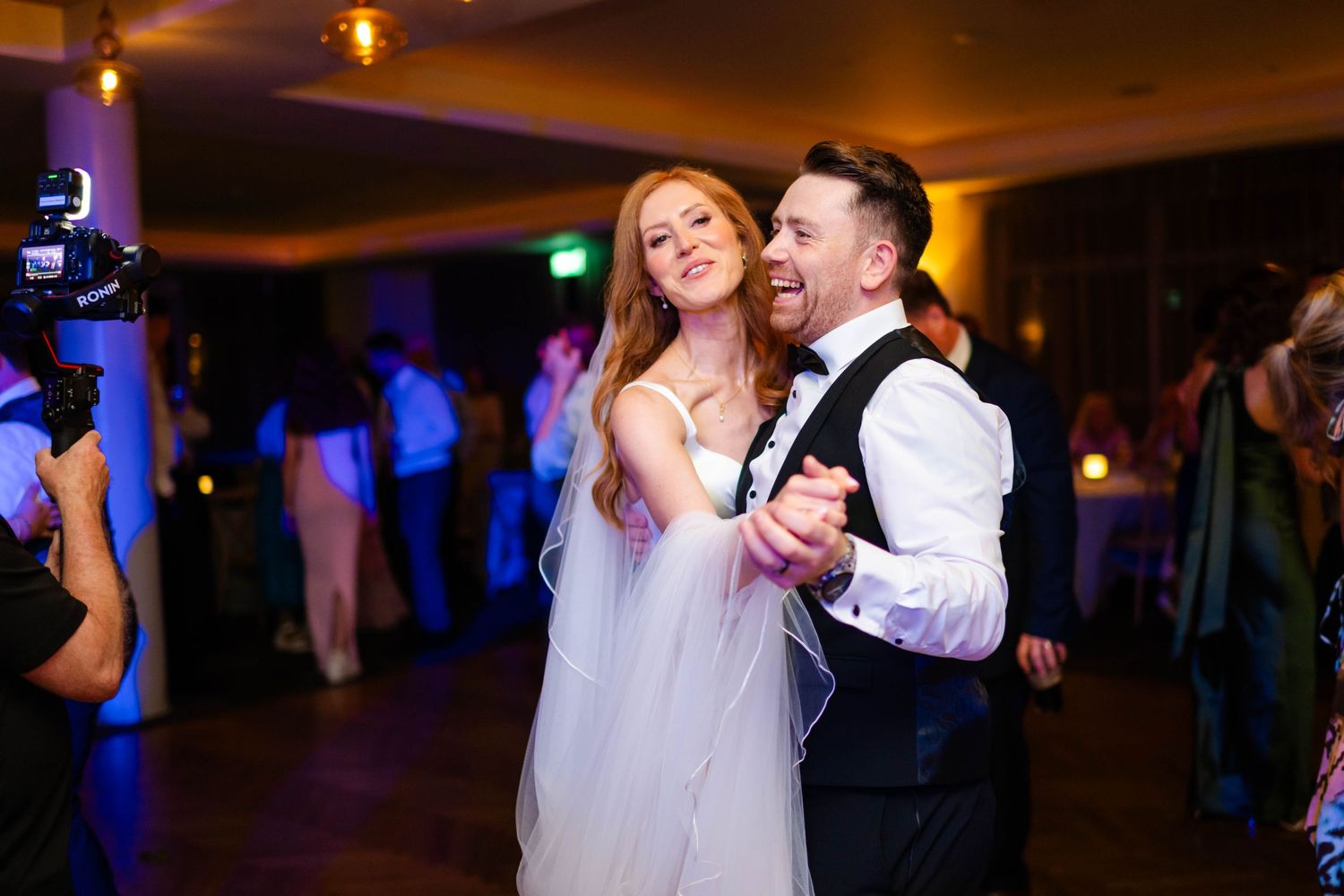 Wedding celebration on dance floor with festive lighting and joyful dancing.