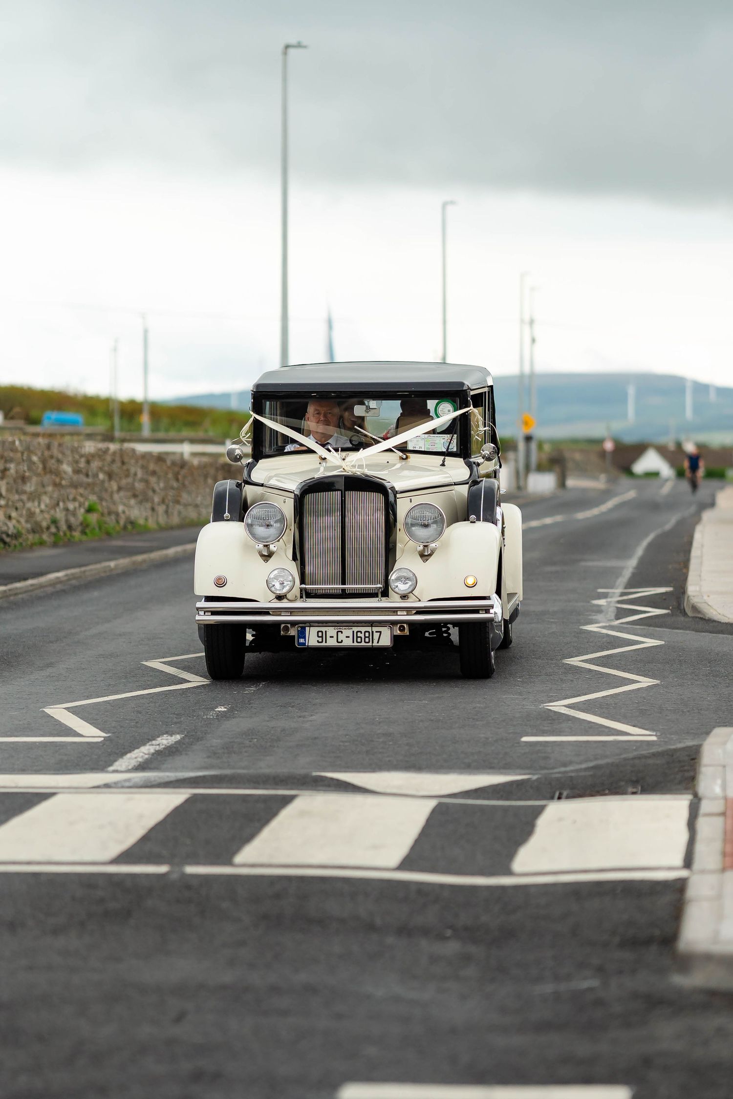 Classic white vintage wedding car parked on an empty road with mountains in the background.