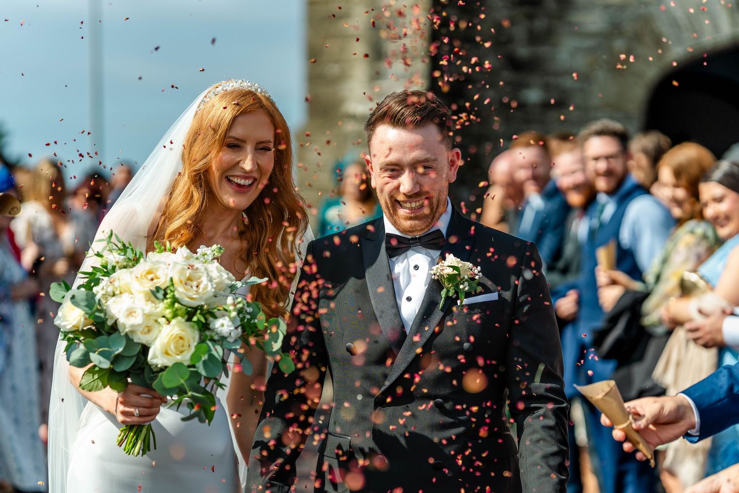 Joyful wedding celebration with confetti being thrown outside a historic stone church.