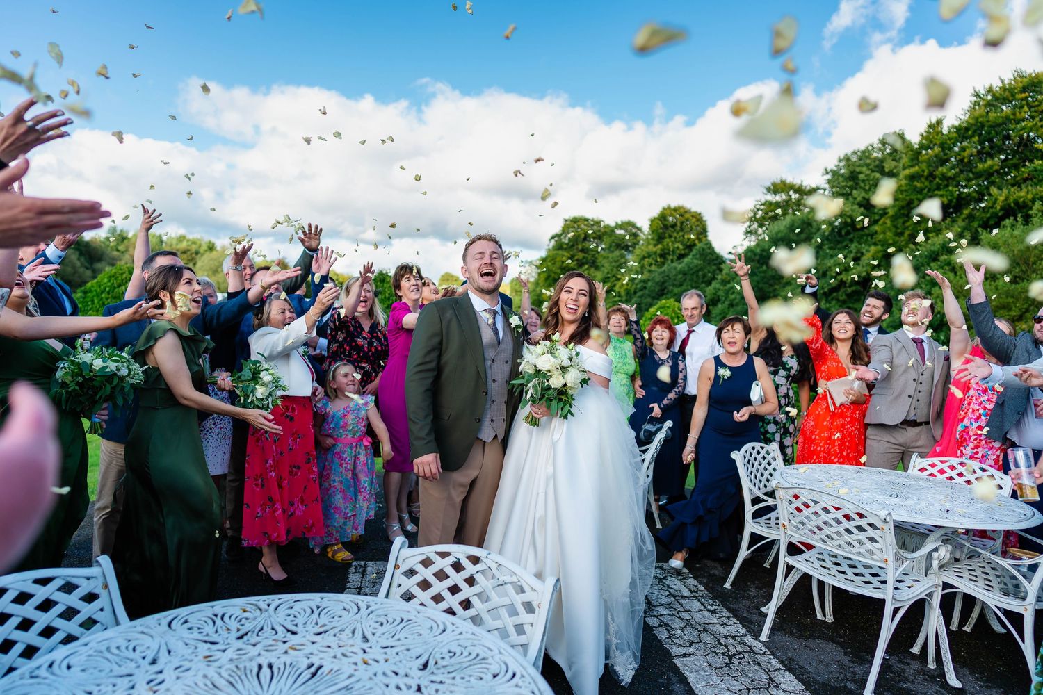 Outdoor wedding reception with confetti toss and guests celebrating on a sunny day.