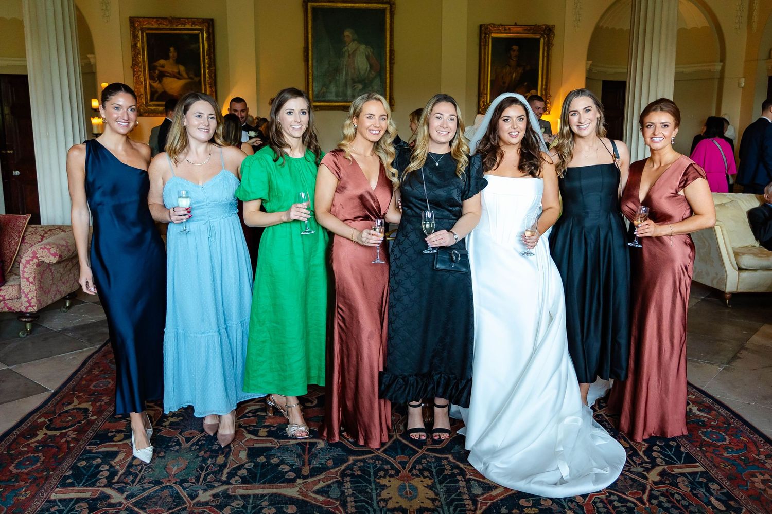 A group of people in formal attire stand together in a line at an elegant indoor venue during a celebration.