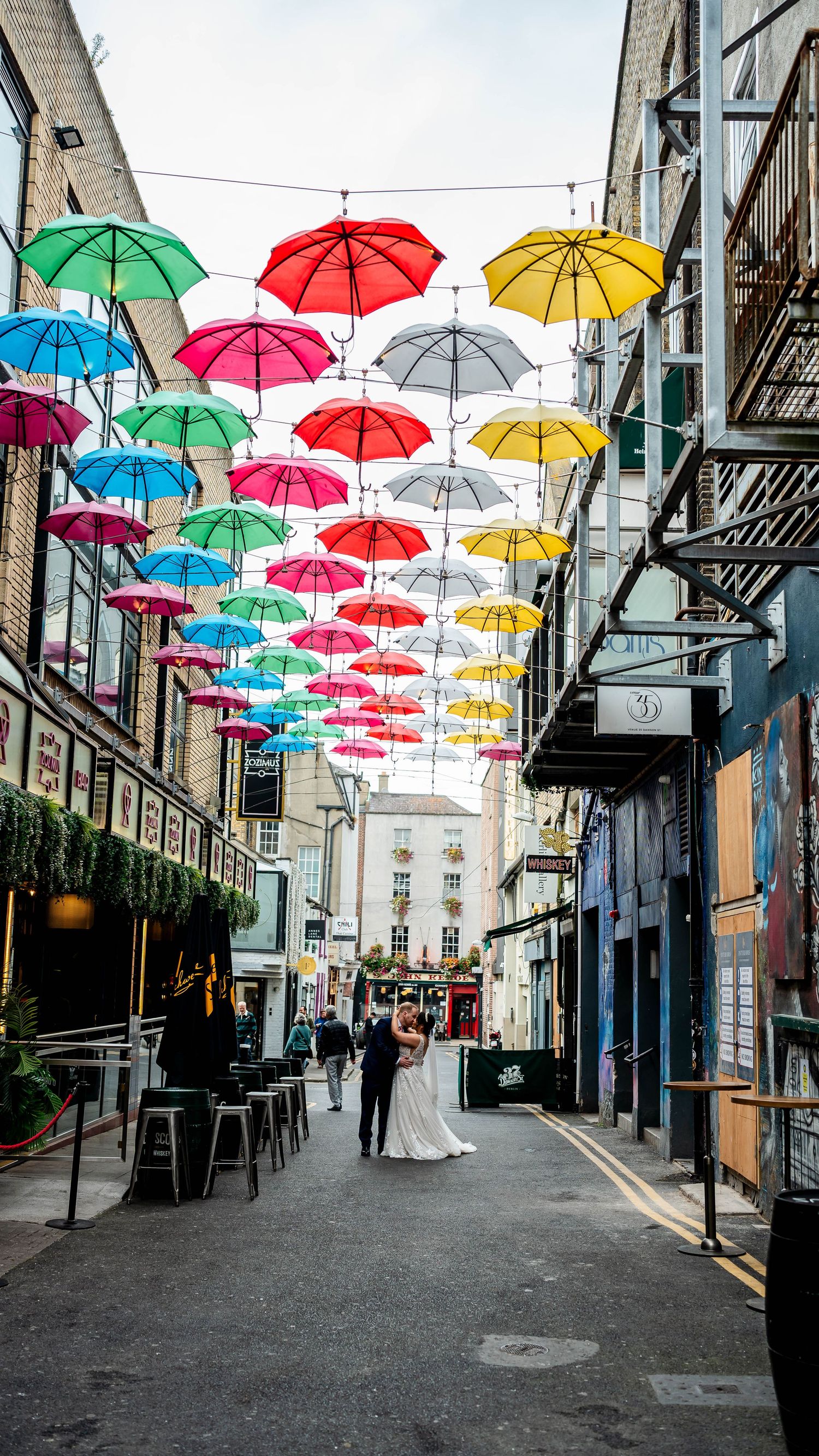 Vibrant suspended umbrellas create a canopy over an urban pedestrian walkway.