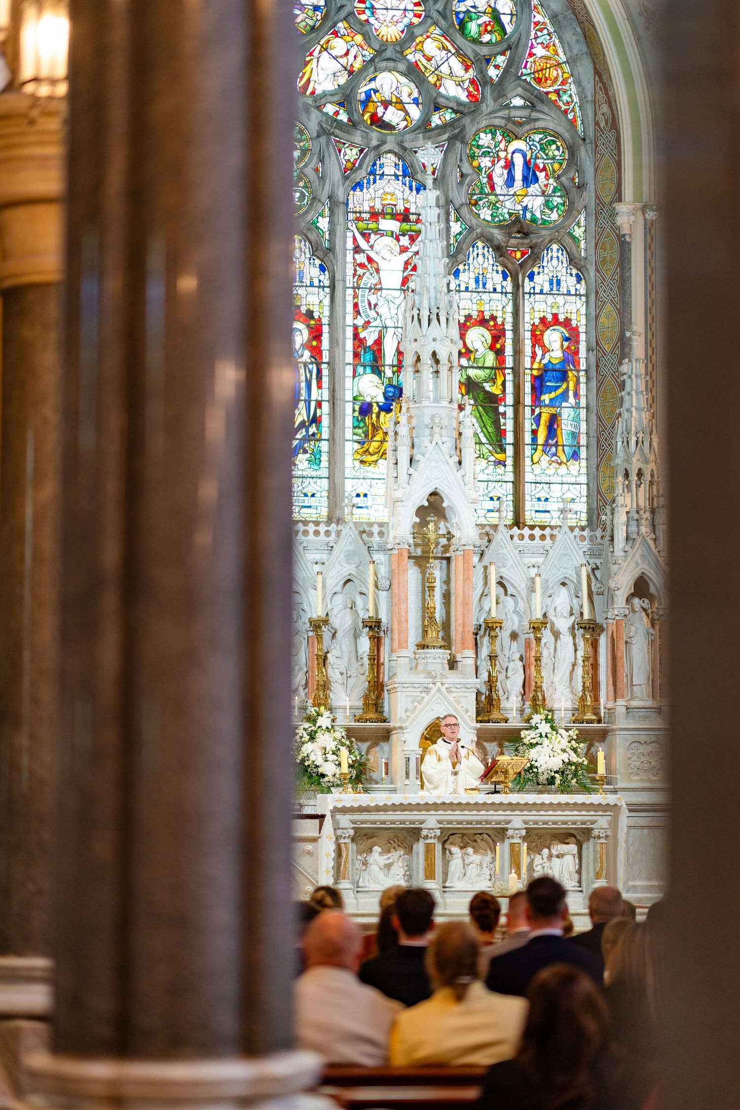 Beautiful stained glass windows and ornate columns inside a historic cathedral with soft lighting and religious decorations.