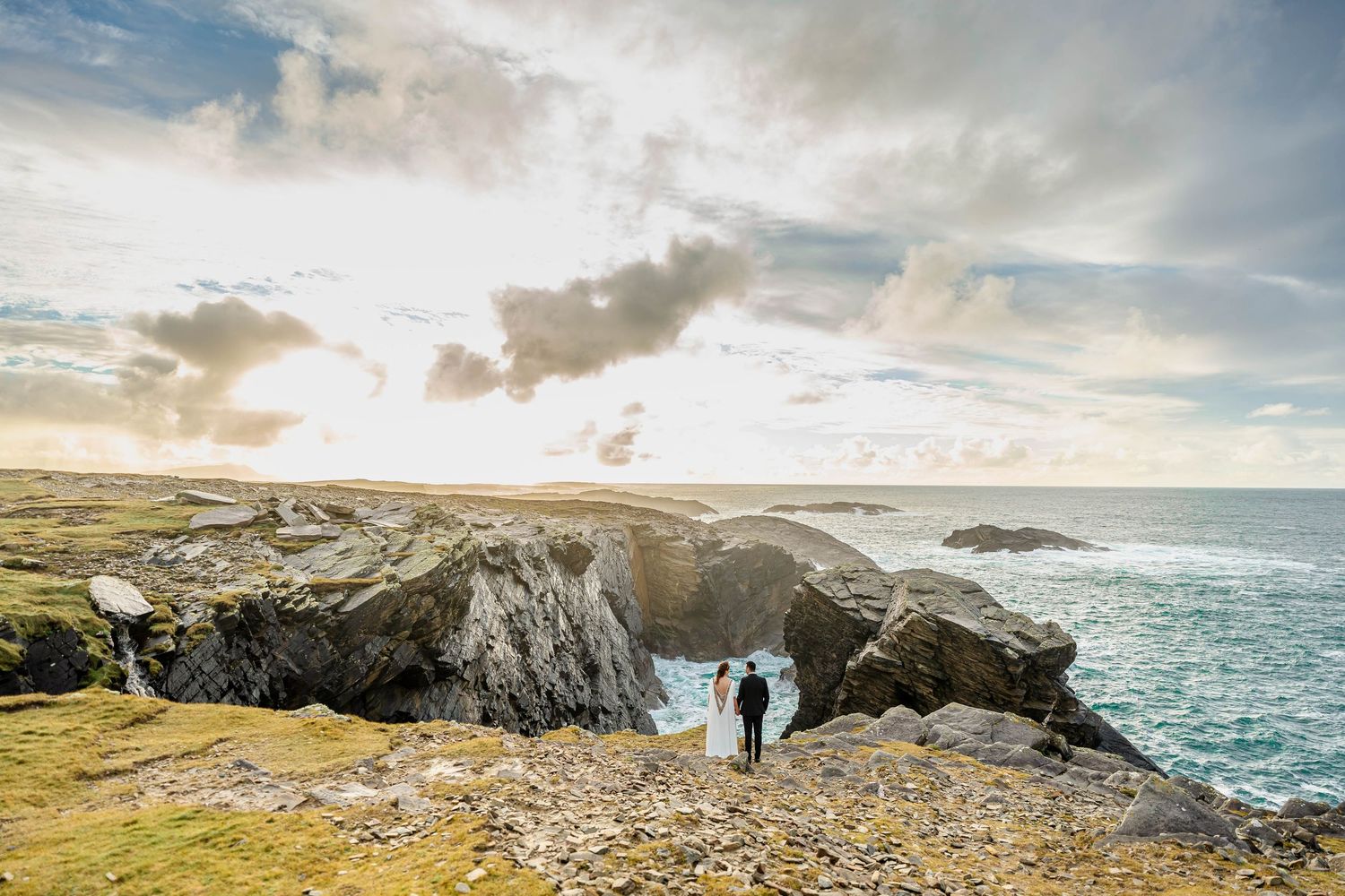 Silhouetted figures on dramatic coastal cliffs during golden hour with ocean views.