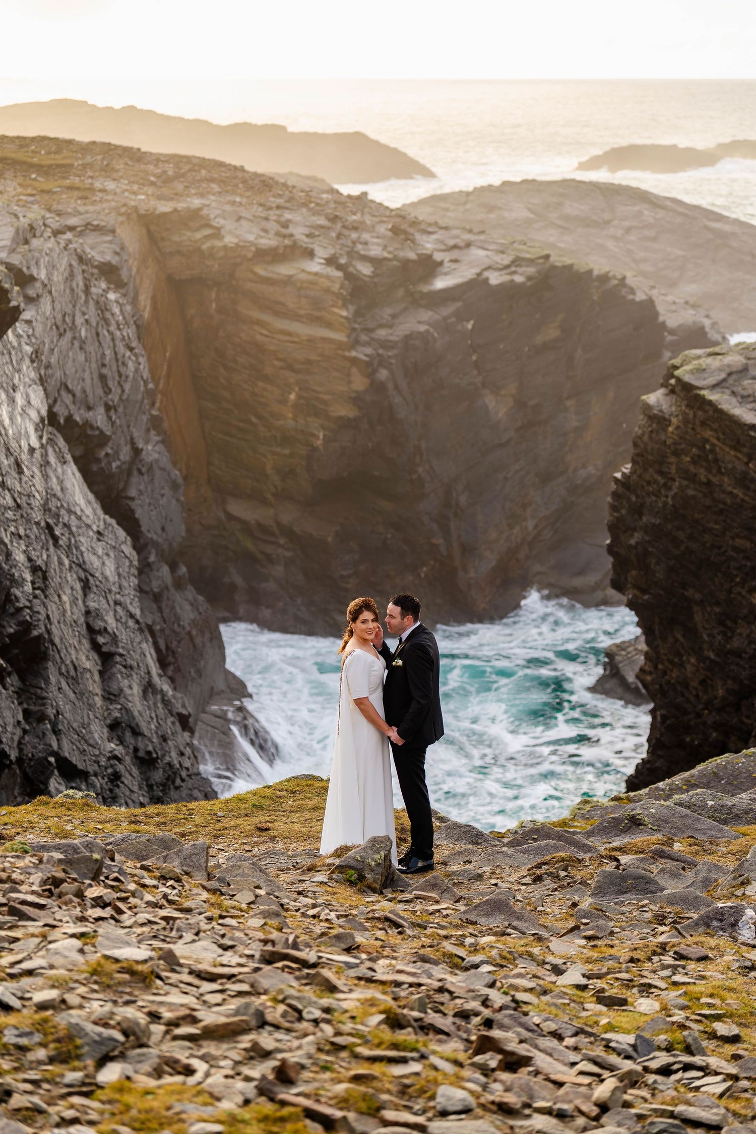 Dramatic wedding photos on rocky cliffs overlooking crashing ocean waves.