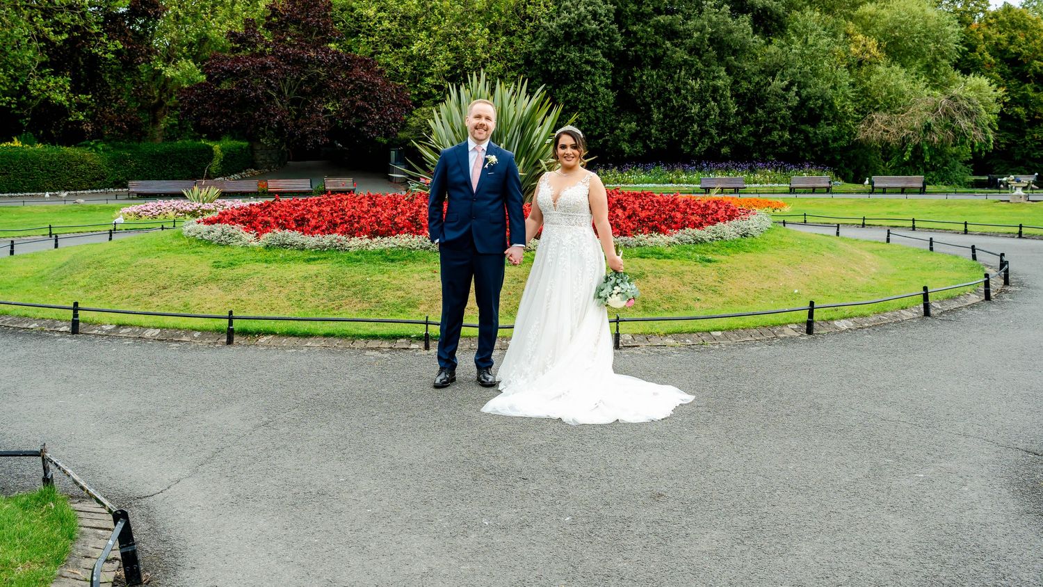 Panoramic view of a park wedding scene with lush greenery and red floral displays.