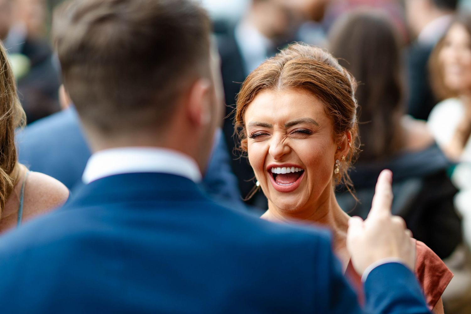 Two people share a joyful moment at an outdoor social gathering, with one wearing a navy blue suit.