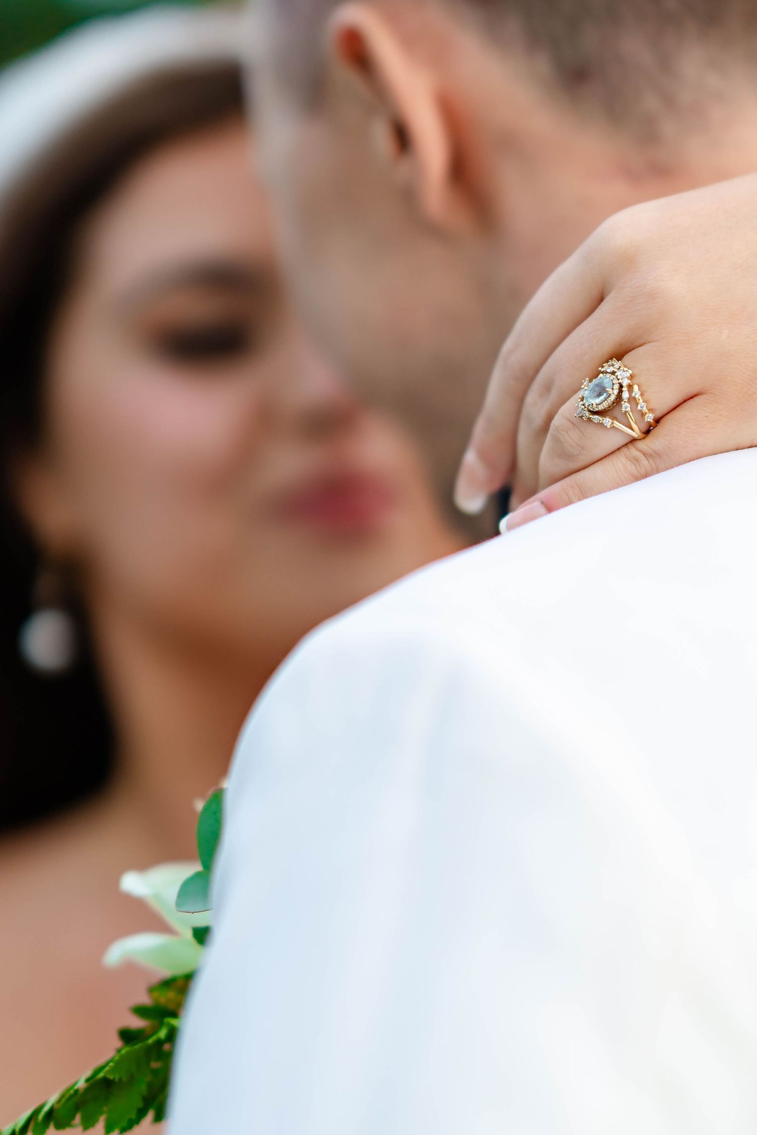 Close-up shot of a diamond engagement ring with delicate detailing against a blurred outdoor background.