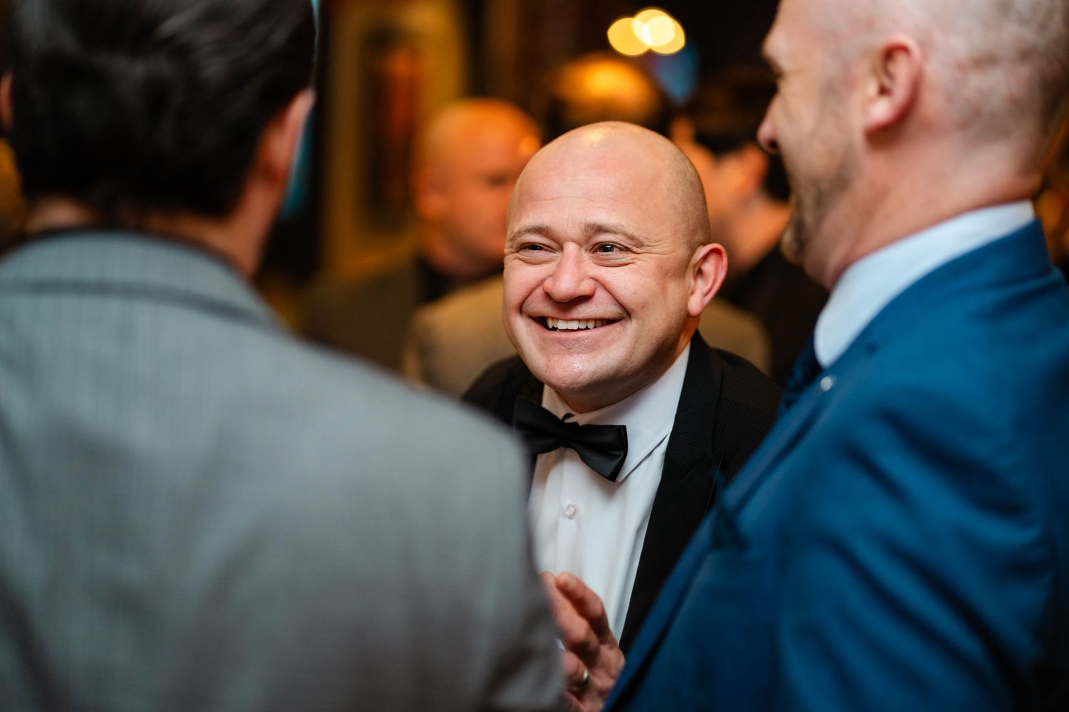 Wedding guests in formal attire mingle and smile during reception.