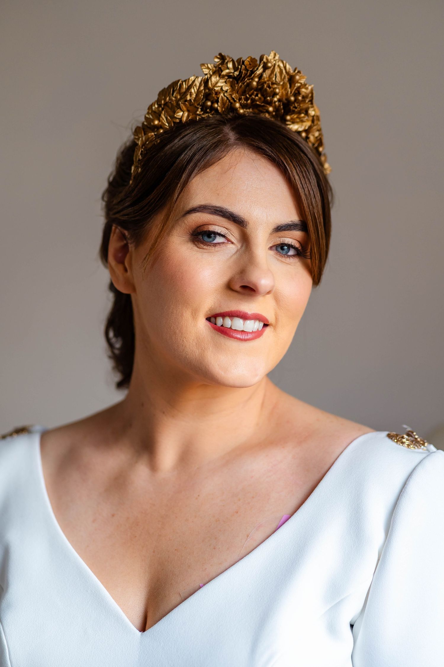 Bride wearing white v-neck dress and gold crown smiling at camera.