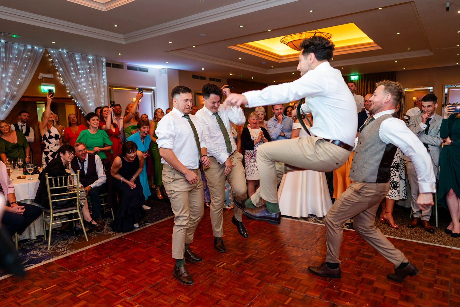Groomsmen perform energetic dance moves during wedding reception on red dance floor.