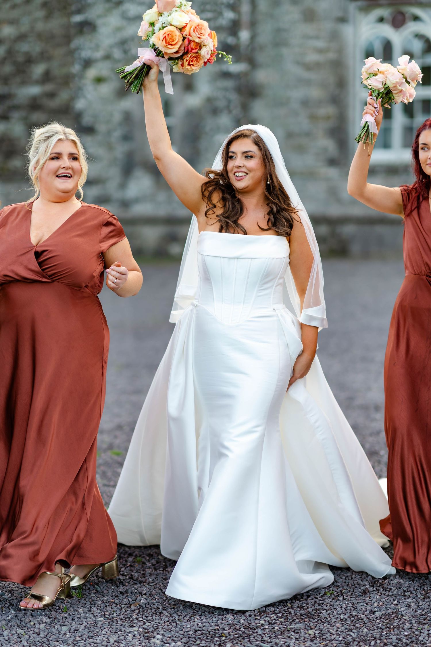 Wedding party in burgundy dresses and white gowns pose together laughing and celebrating outdoors.