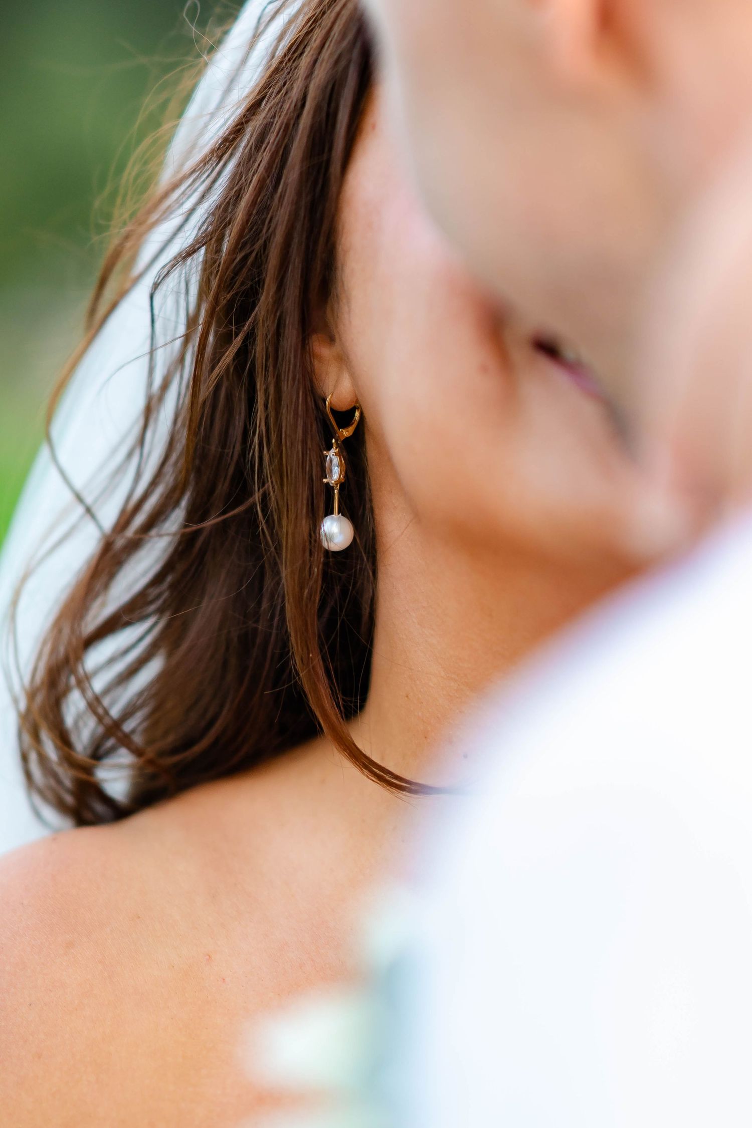 Close-up view of an elegant pearl drop earring on a woman's ear with soft brown hair in the background.
