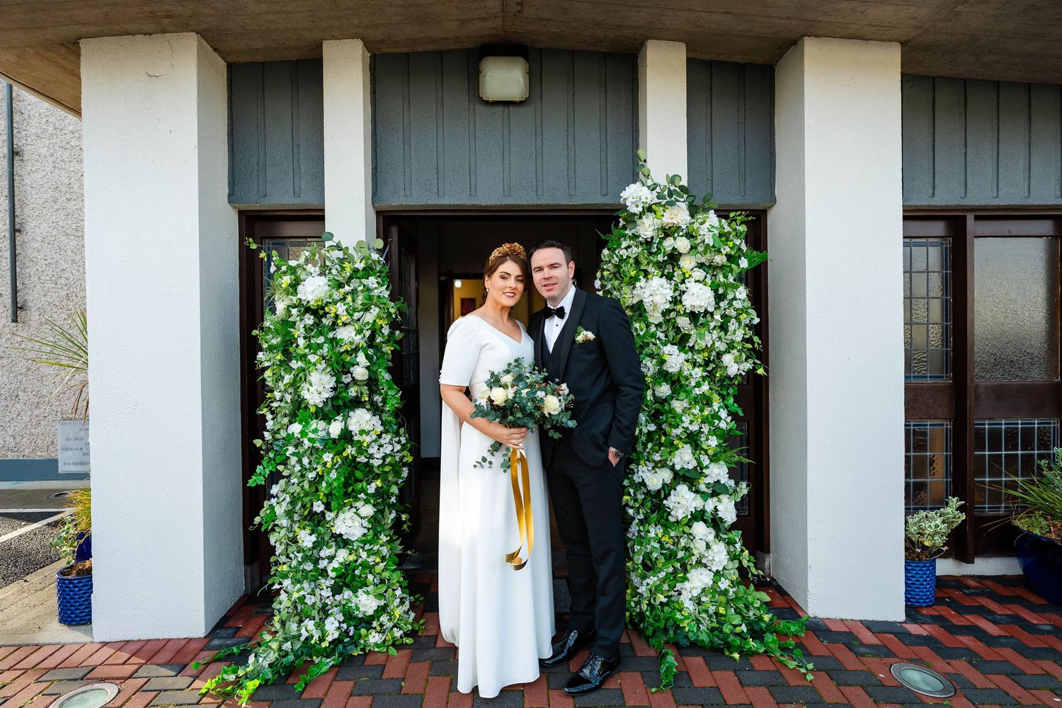 Outdoor wedding portraits taken under architectural columns with greenery.