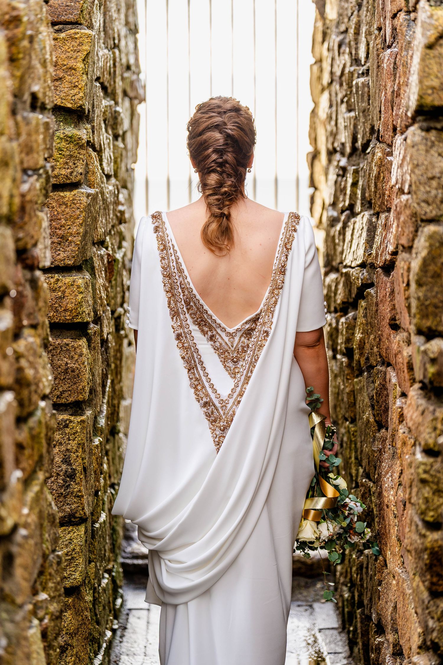 Elegant beaded V-back wedding dress detail shown through stone archway.