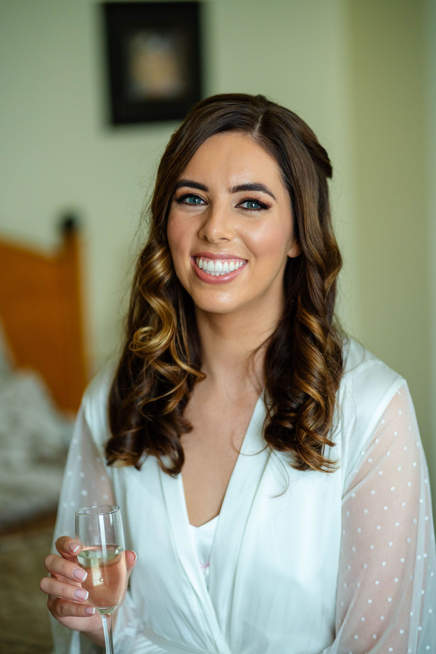 A radiant bride in a white polka dot robe smiles while getting ready on her wedding morning.