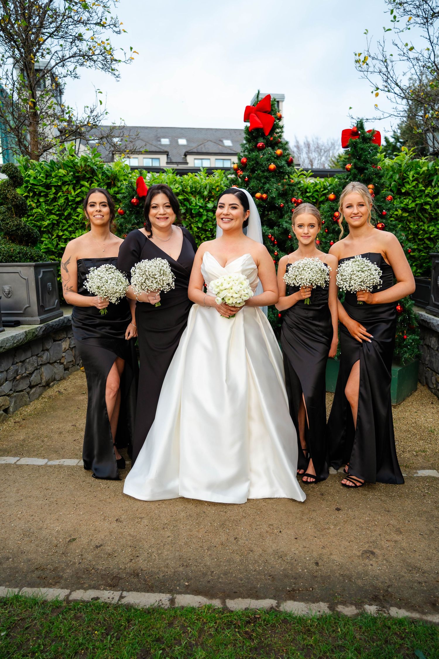 Bridal party poses in garden with bridesmaids wearing black gowns and bride in white wedding dress.