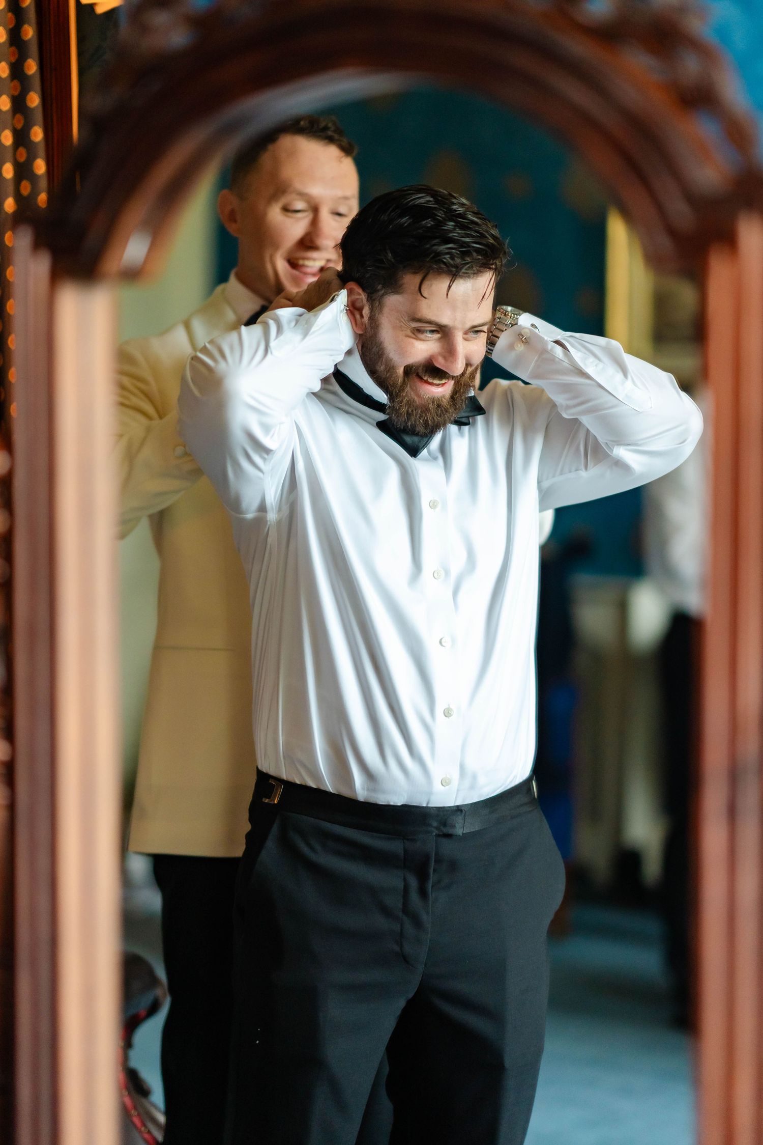 A person in formal attire smiles and poses against a wooden architectural backdrop.