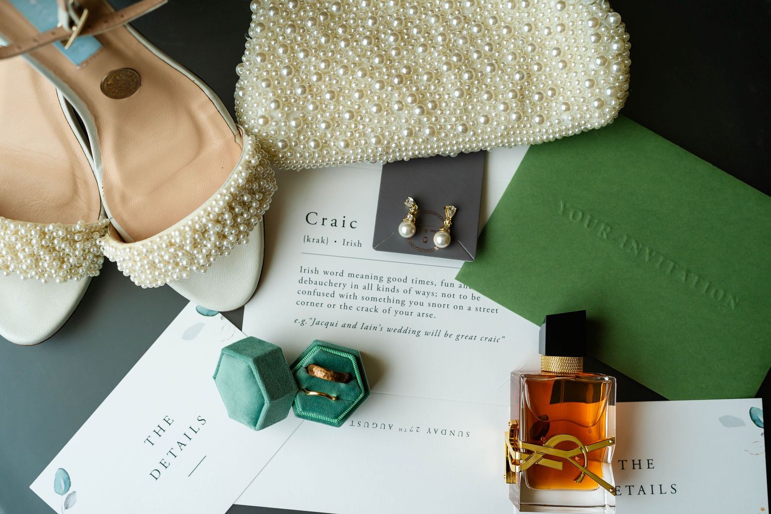 Wedding details including pearl-encrusted accessories and invitation on green background.