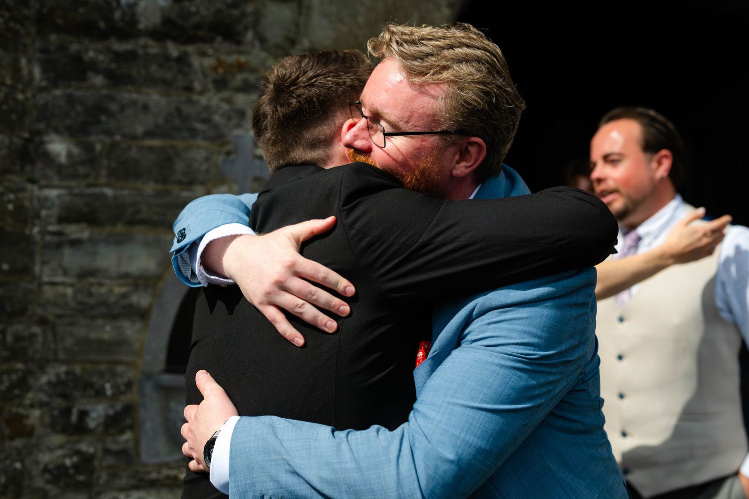 Series of emotional hugs and embraces taking place outside a stone church building.