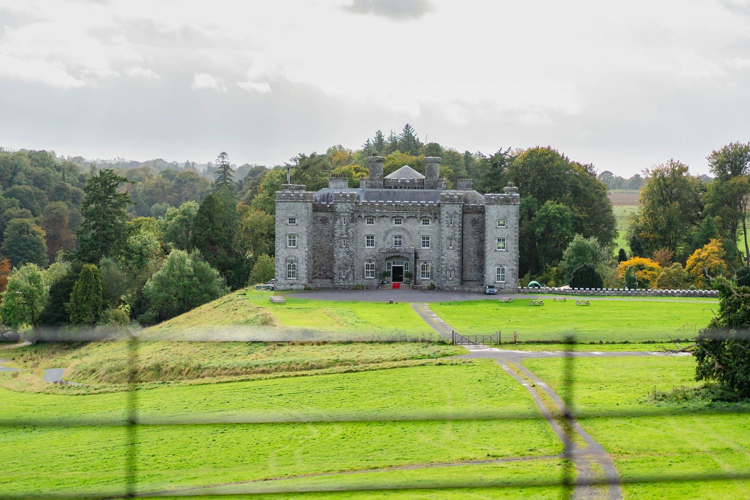 Panoramic view of a historic stone mansion set against rolling green lawns and lush countryside landscape.