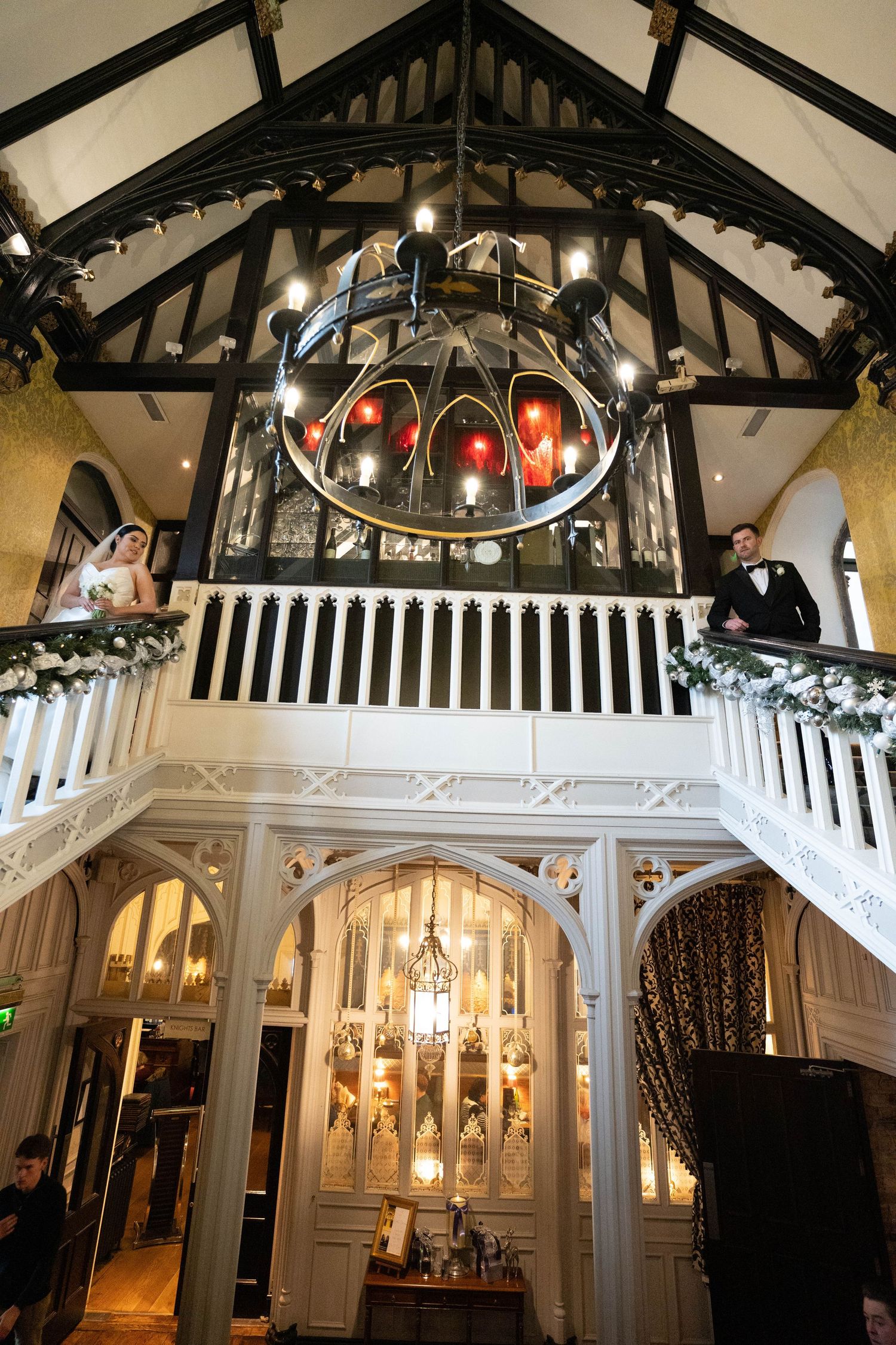 An ornate wedding venue interior featuring dramatic lighting, wooden beams, and decorated balconies.