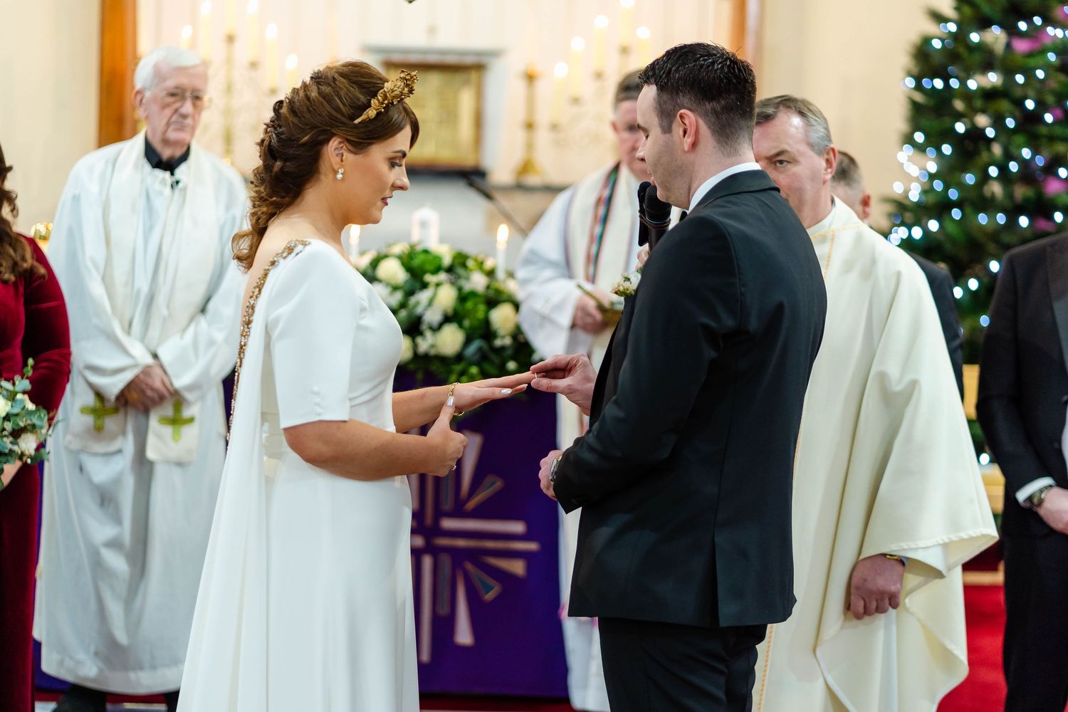 Wedding ceremony in church with Christmas trees and holiday decorations visible.