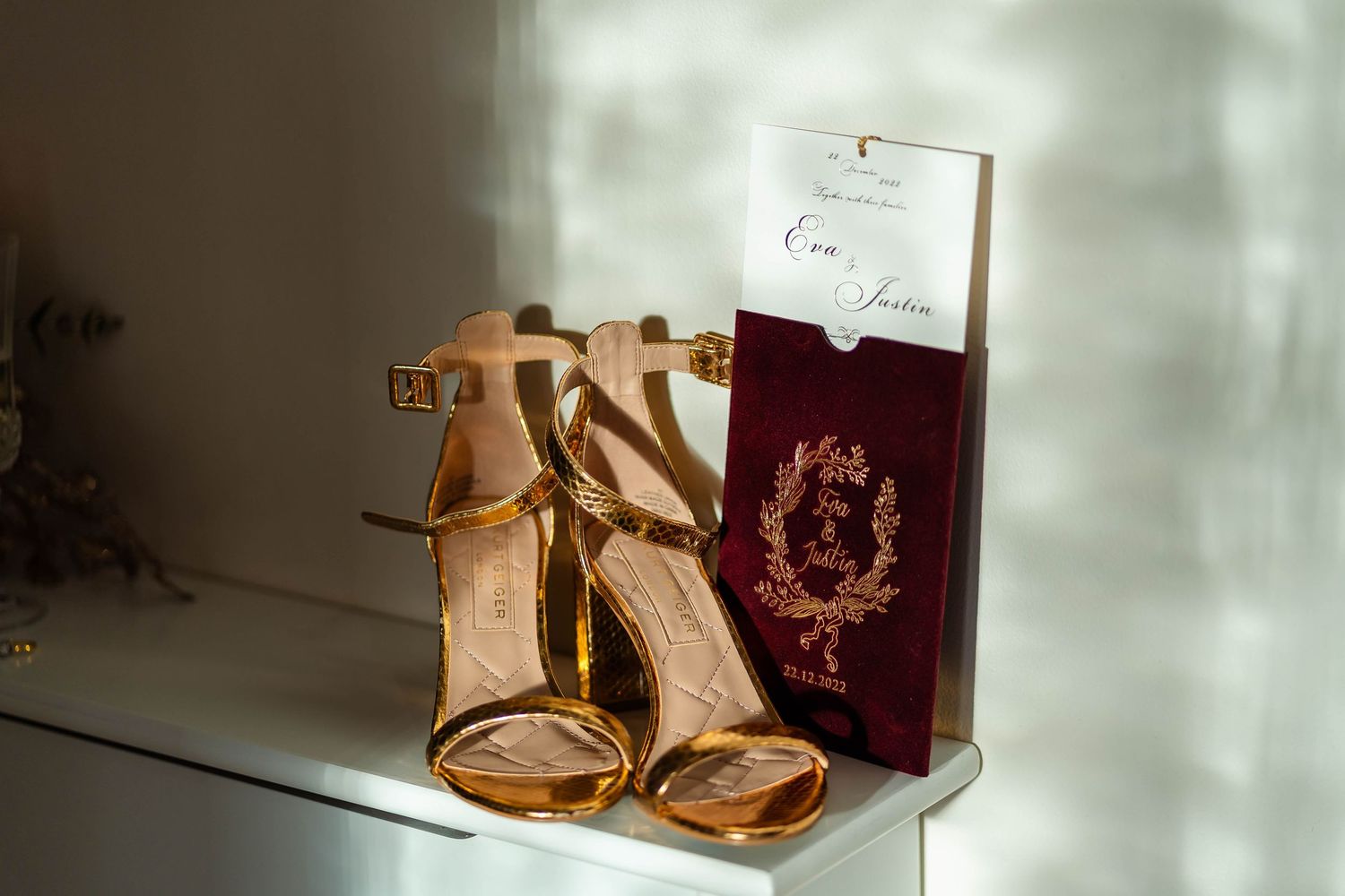 Elegant gold wedding shoes displayed with burgundy passport and invitation.