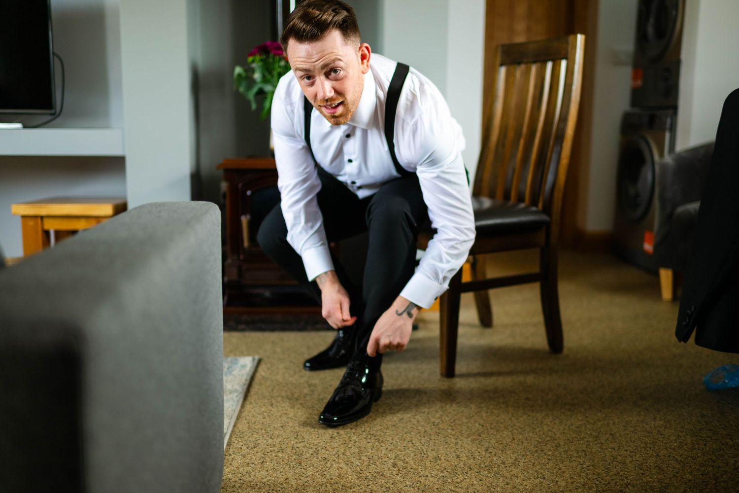 Man in white dress shirt getting ready for formal event on carpeted floor.