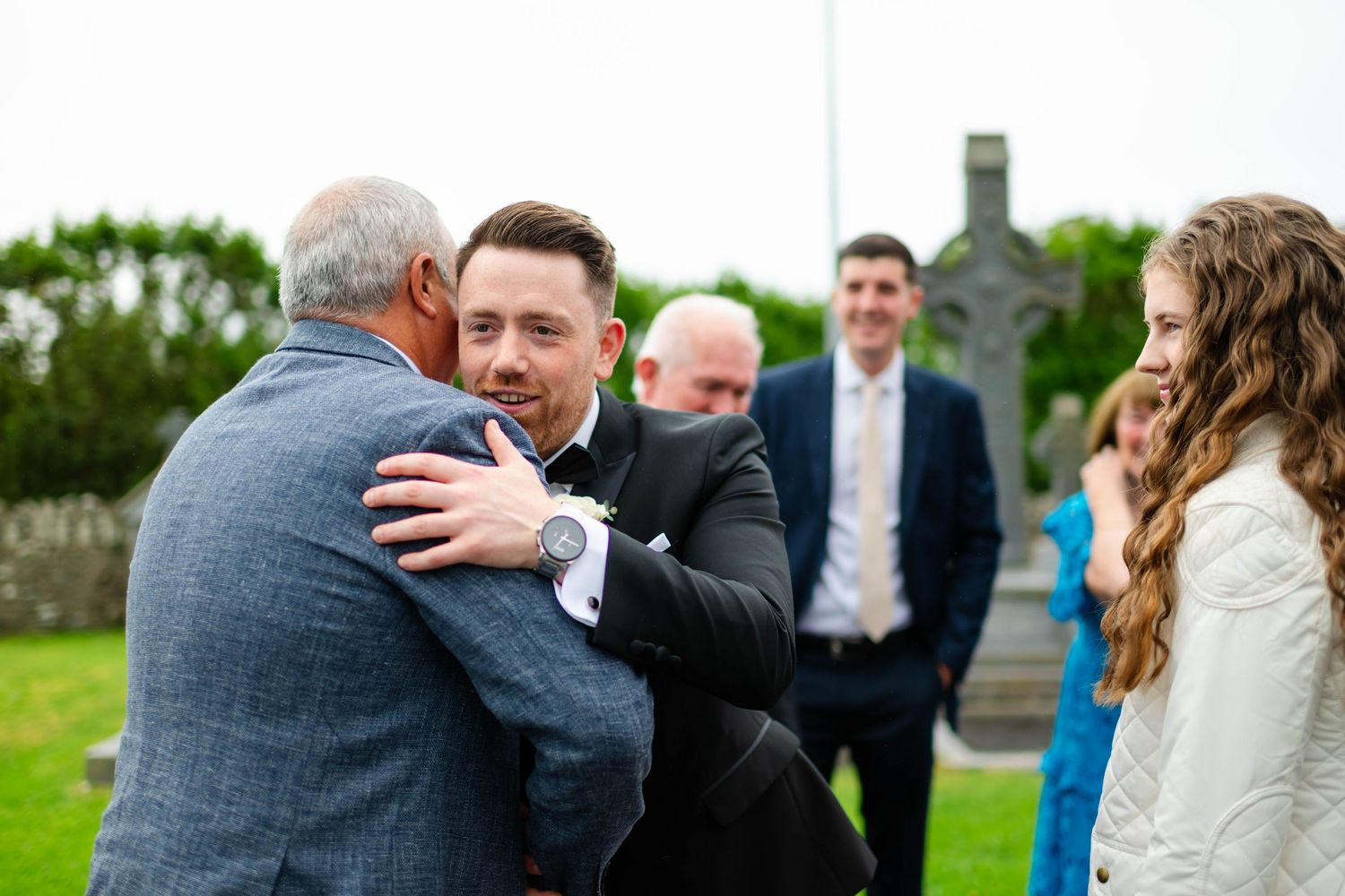 Wedding guests sharing emotional embraces outdoors on a cloudy day.