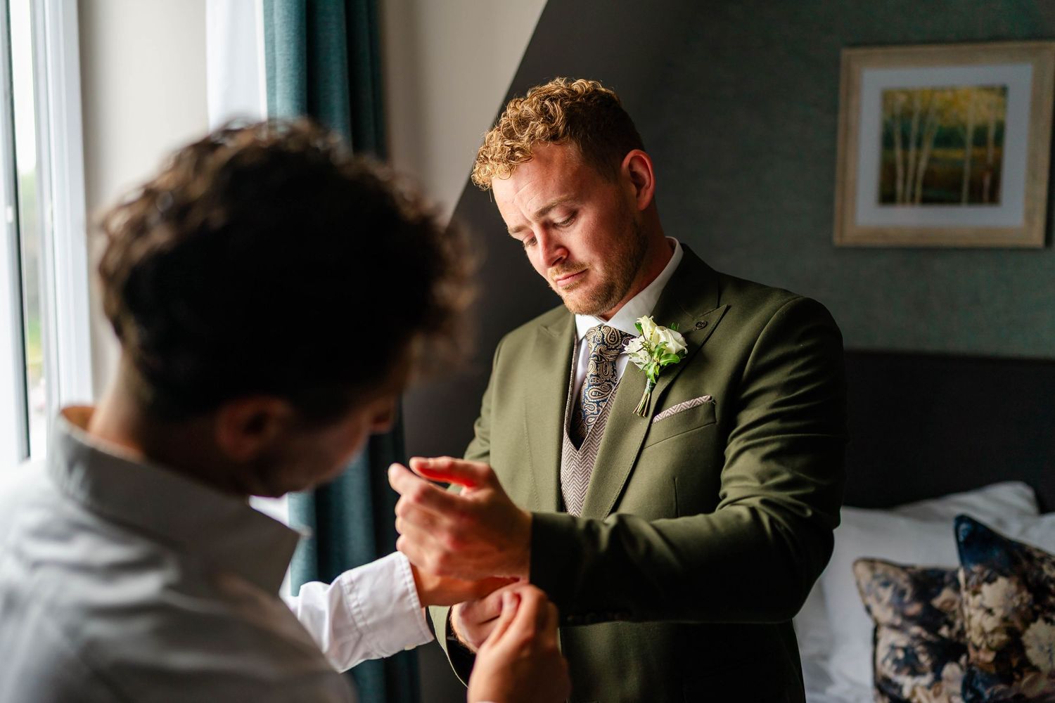 Person in formal attire reads letter near window with emotional expression.