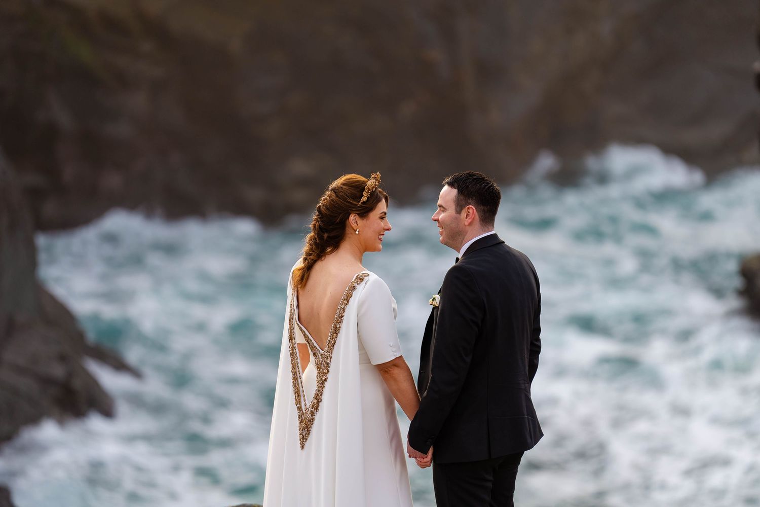 Elegant wedding couple shares intimate moment against dramatic coastal backdrop.