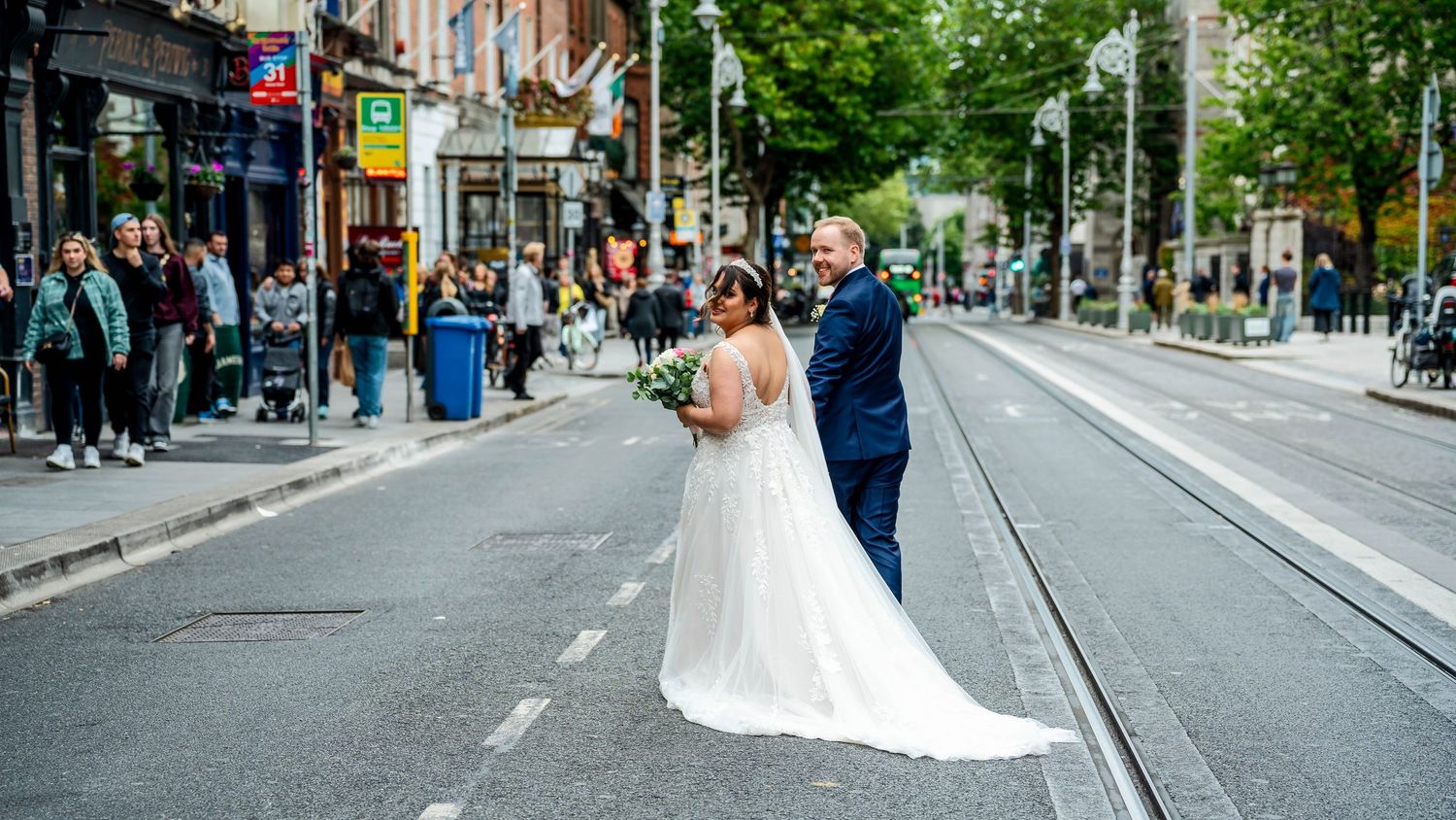 Urban wedding scene on a city street with tram lines and buildings in the background.