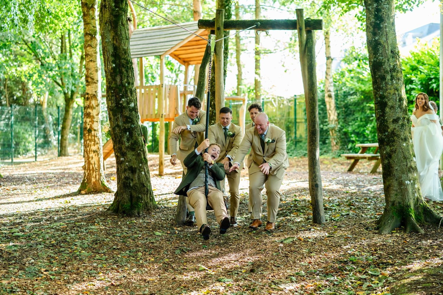 Wedding party takes casual photos under a canopy of trees.