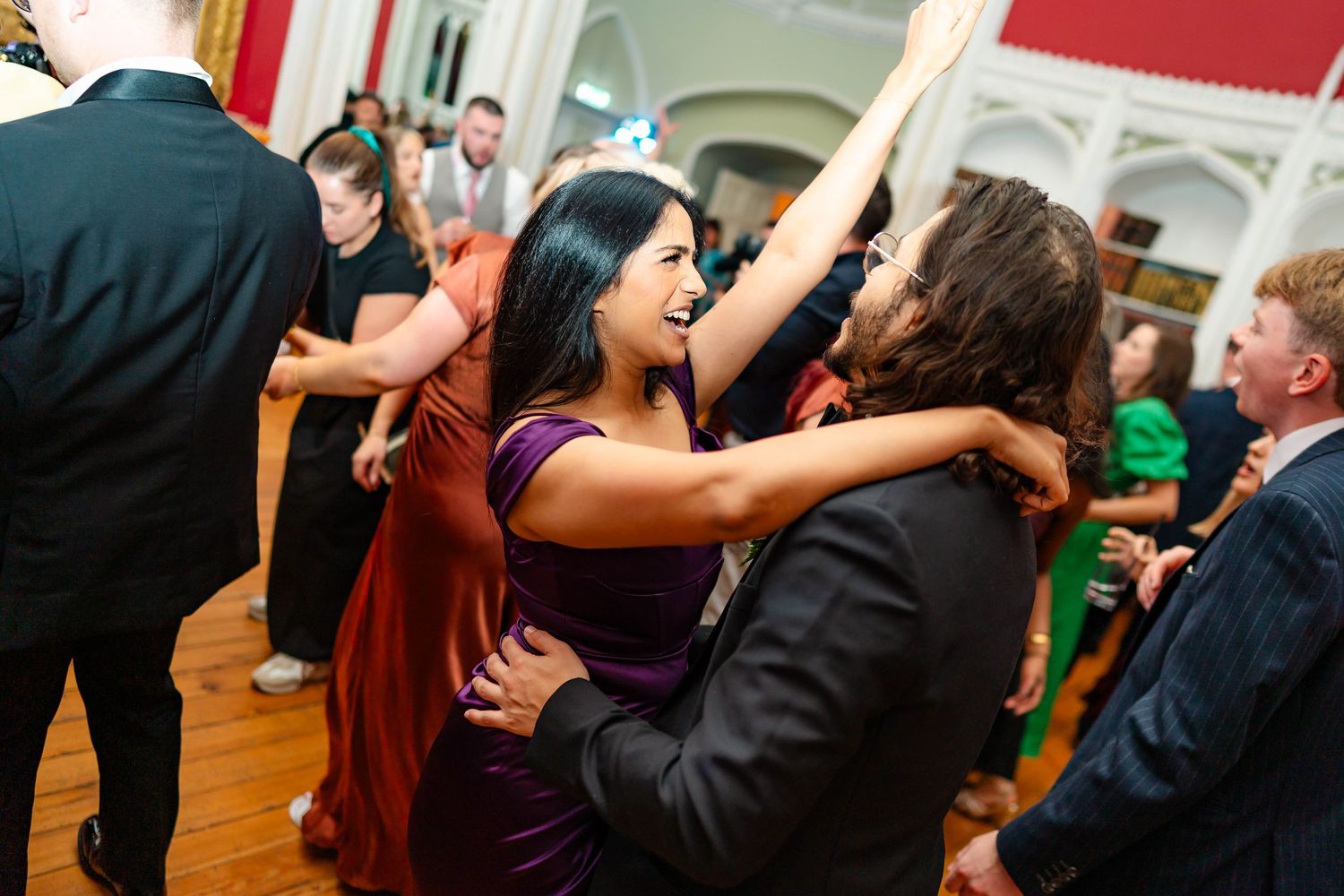 Wedding guests dancing and celebrating together on a wooden dance floor during an indoor reception.